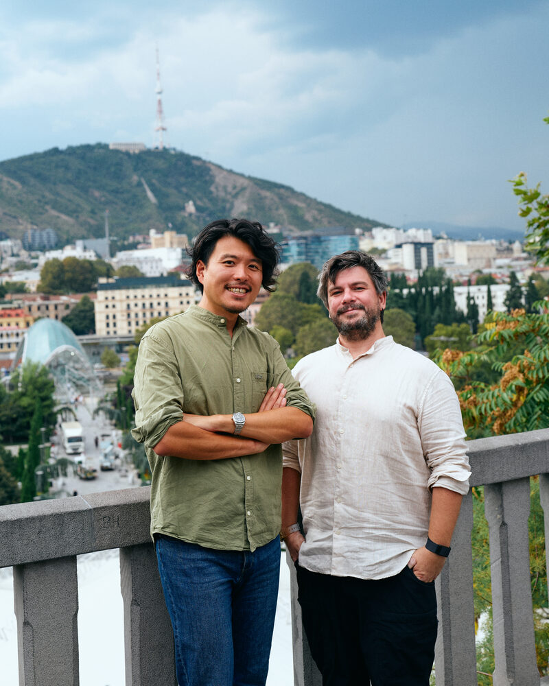 Toshiki Asano and Tornike Tvalavadze standing side by side with the city of Tbilisi behind them